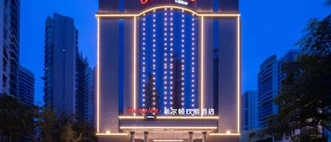 A hotel with a prominent 'Hampton by Hilton' sign, large windows, and a well-lit entrance.