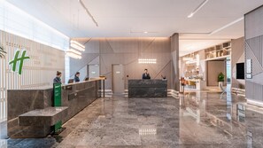 Een moderne hotellobby met een receptiebalie, een wachtruimte en een trap naar de bovenverdiepingen.