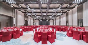 Een ruime congreszaal met ronde tafels, rode stoelen en een modern plafondontwerp.