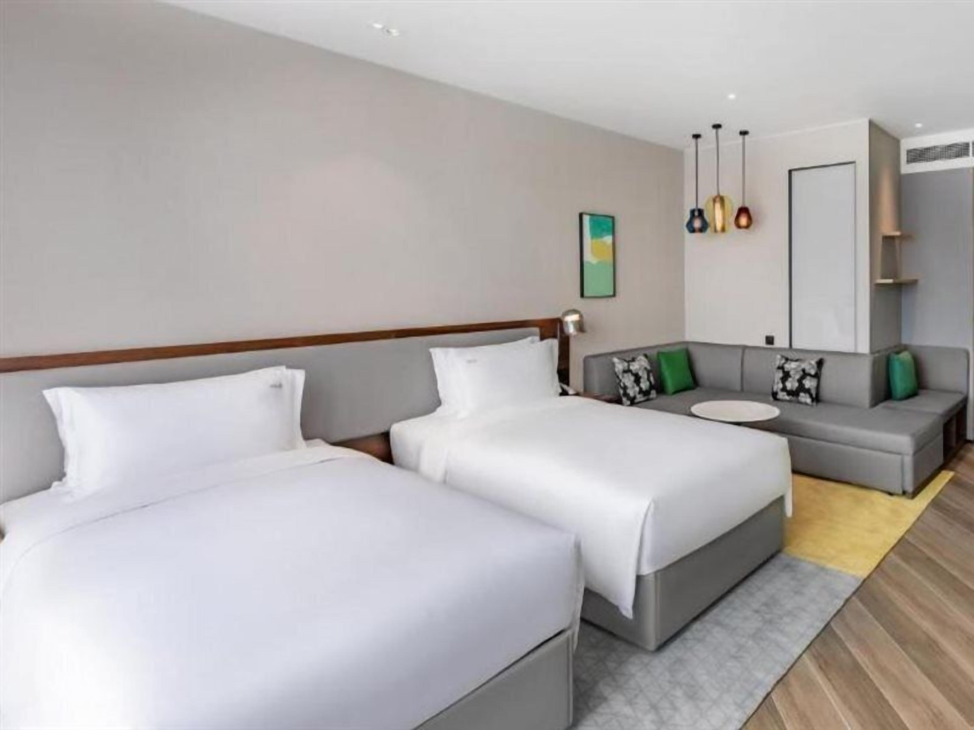 Ein modernes Hotelzimmer mit zwei Betten, einem Sofa und einem kleinen Tisch.