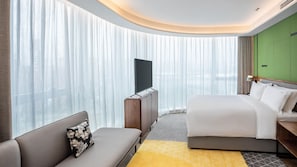 A hotel room with a bed, a sofa, a TV, and a green accent wall.