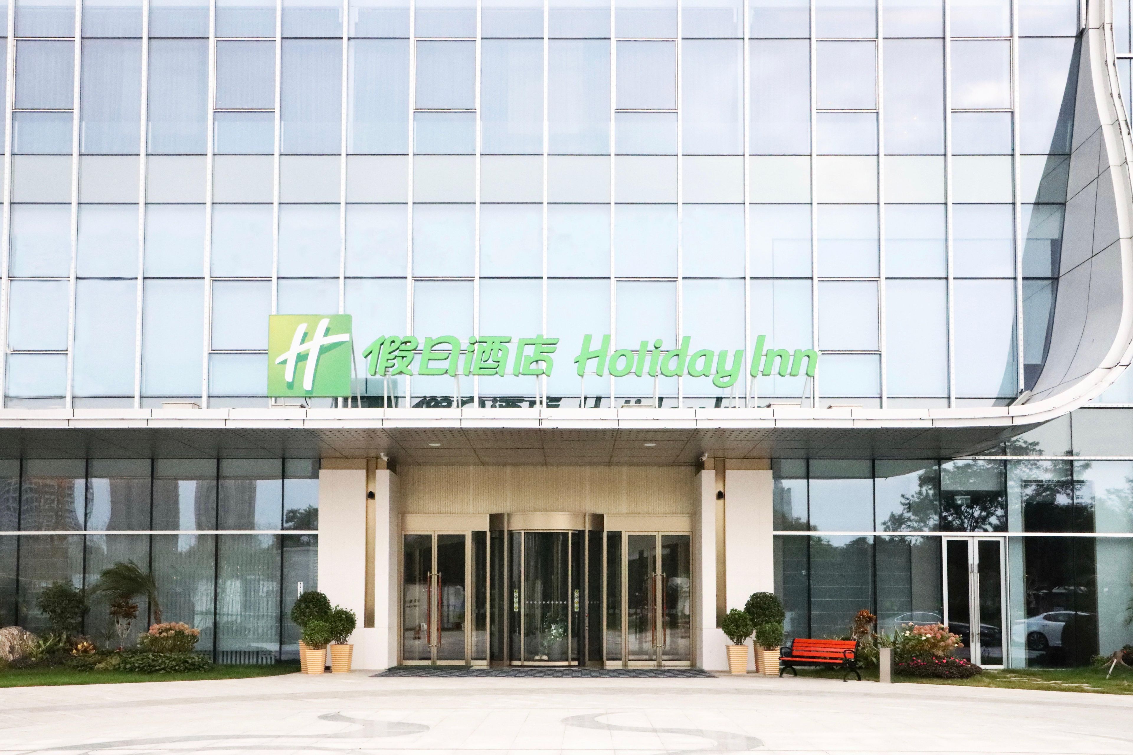 Een modern gebouw met een Holiday Inn bord, grote glazen ramen en een verzorgd entreegebied.