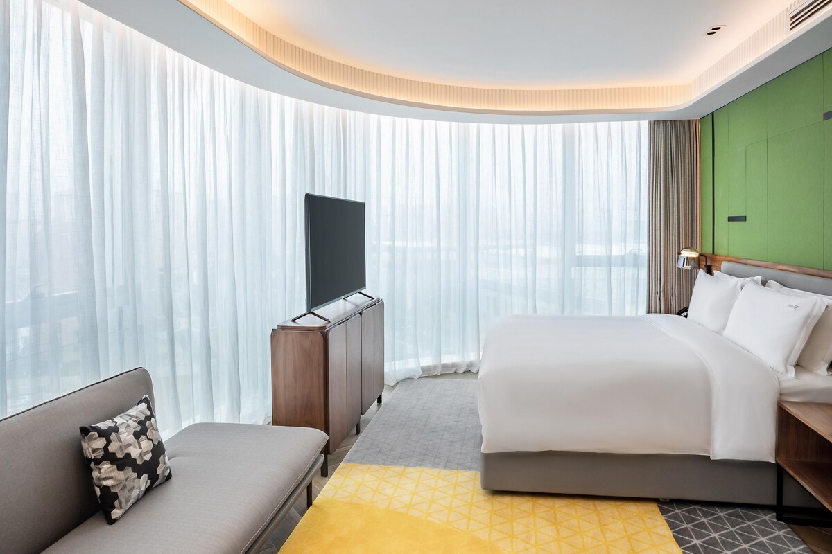 Een hotelkamer met een bed, een bank, een televisie en een groene accentmuur.