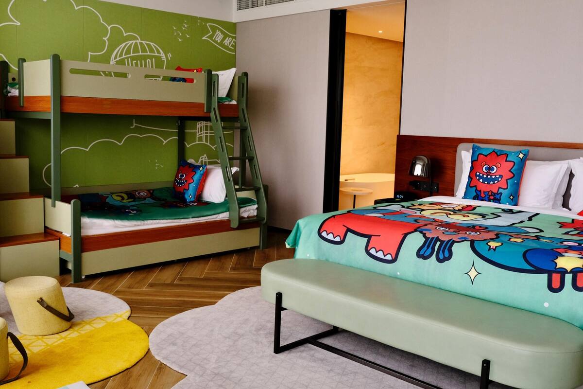 A bunk bed with a green wall, a small table, and a bench.