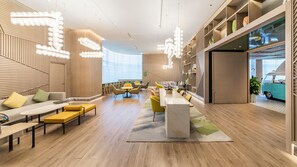 A modern interior with a long dining table, yellow chairs, and a seating area with sofas and a bench.