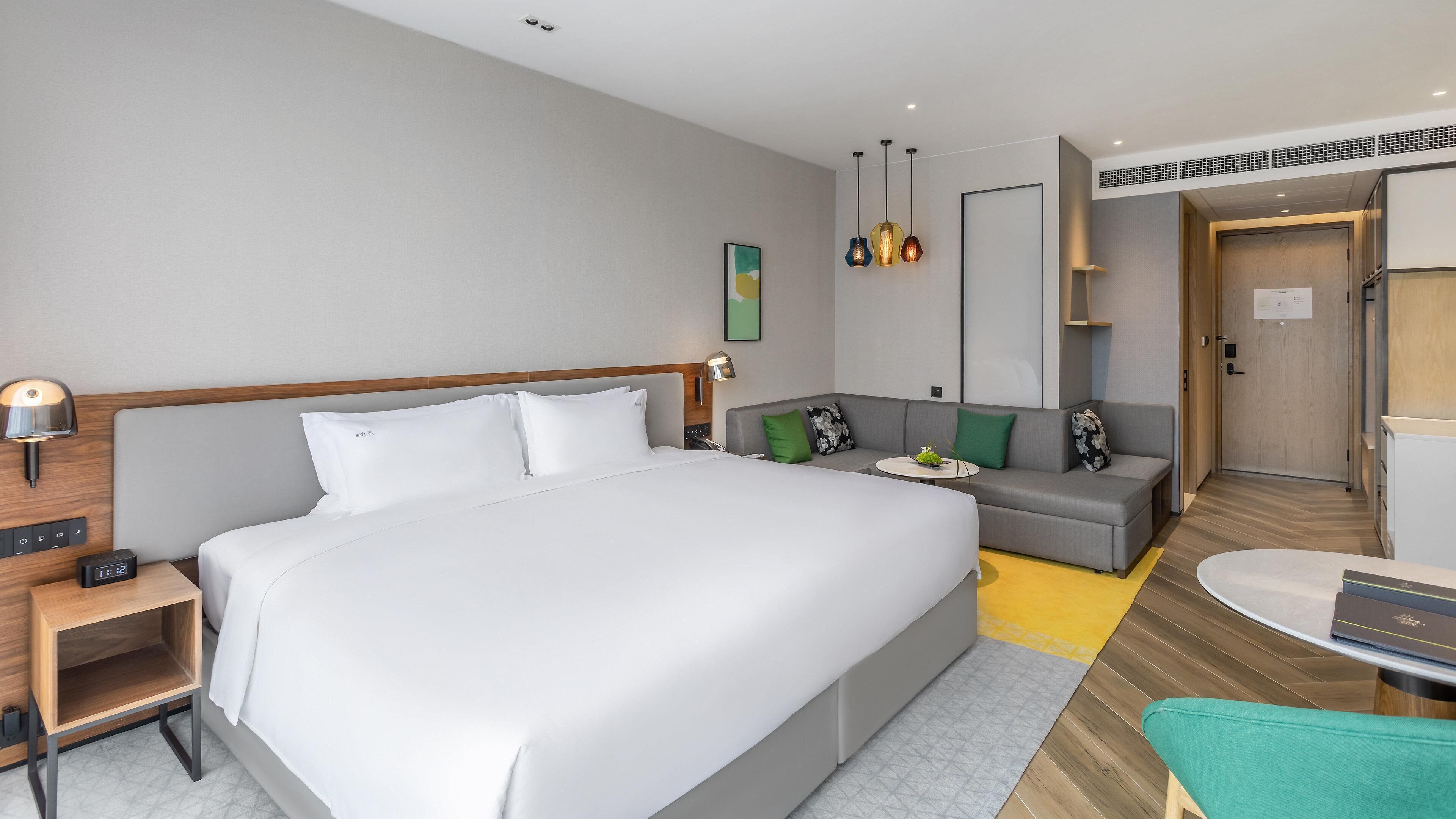 A modern hotel room with a large bed, a sofa, a small table, and a desk.