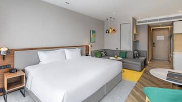 A modern hotel room with a large bed, a sofa, a small table, and a desk.