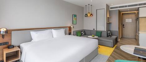 A modern hotel room with a large bed, a sofa, a small table, and a desk.