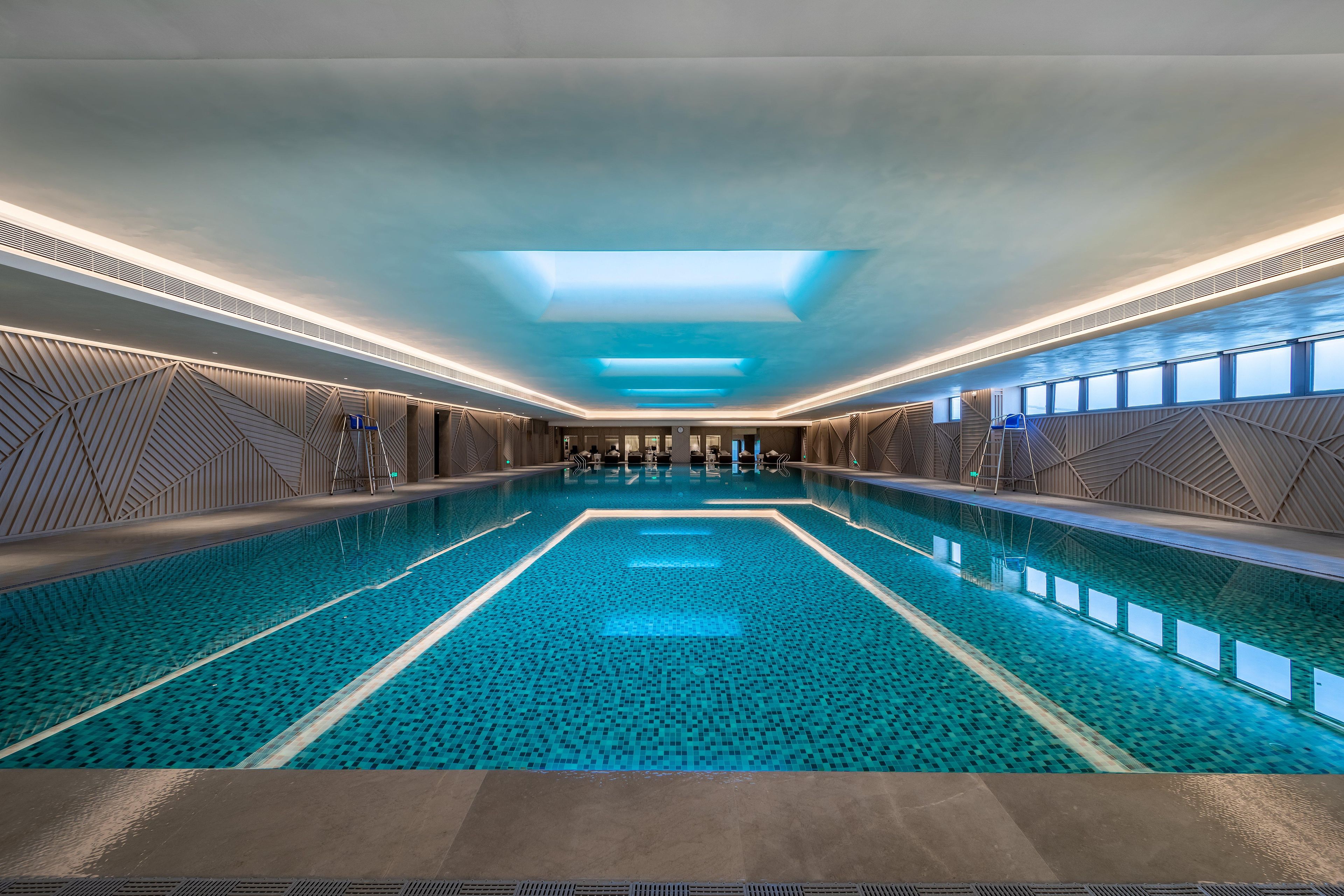 Une grande piscine intérieure dotée de motifs géométriques sur les murs et de lucarnes.