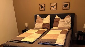 Cama bem arrumada com colcha xadrez, dois travesseiros e mesa de cabeceira com abajur.