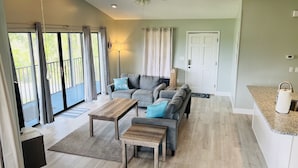Ein geräumiges Wohnzimmer mit grauem Sofa, Couchtisch aus Holz und Deckenventilator.