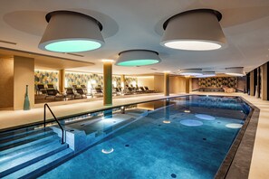 A modern indoor swimming pool with lounge chairs and a sunbed area.