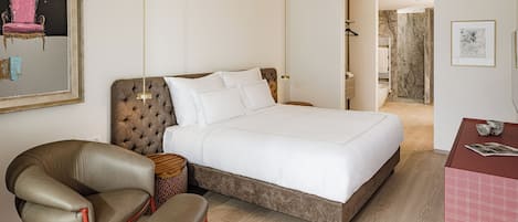 A hotel room with a large bed, a chair, a table, and a mirror.