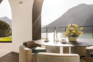 A round table with chairs, a vase of flowers, and a bottle on a balcony overlooking a lake and mountains. - Aria Retreat & SPA (Porlezza)