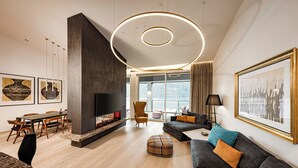 A modern living room with a fireplace, a large sofa, a dining area, and a large window offering a view.