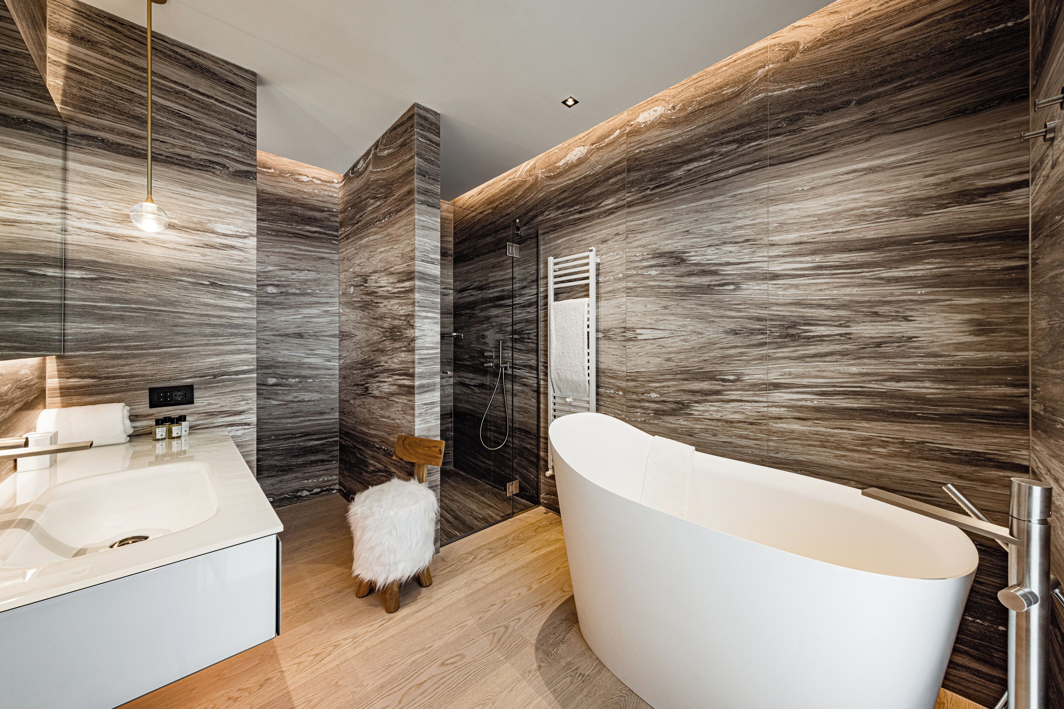 Une salle de bain moderne avec une baignoire sur pieds, une douche en verre et un mur à l’aspect marbré.