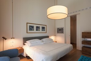 Une chambre à coucher comprenant un lit, des tables de chevet, une chaise, un luminaire suspendu et des œuvres d’art encadrées accrochées au mur.