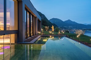 A modern building with large windows, a reflective pool, and a mountainous landscape in the background.