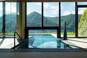 A modern indoor pool with a glass barrier, large windows, and a view of green mountains. - Aria Retreat & SPA (Porlezza)