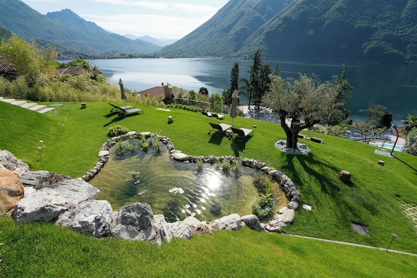 Un jardin paisible au bord du lac, avec un étang, des chaises longues et un sentier en pierre.