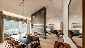 A modern dining area with a long table and chairs, a fireplace, and a sofa in the background.