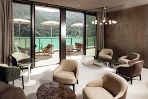 A modern hotel room with a balcony, furnished with chairs and tables, large windows offering a view of a lake and mountains. - Aria Retreat & SPA (Porlezza)