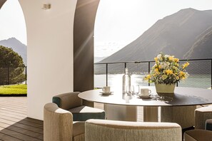 A round table with chairs, a vase of flowers, and a bottle on a balcony overlooking a lake and mountains. - Aria Retreat & SPA (Porlezza)