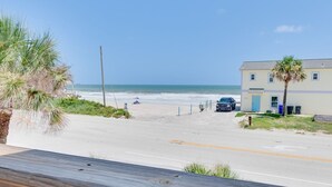 Blick auf einen Strand mit einer Straße, die zu einem Gebäude mit einer blauen Tür führt, Palmen und einem klaren Himmel.