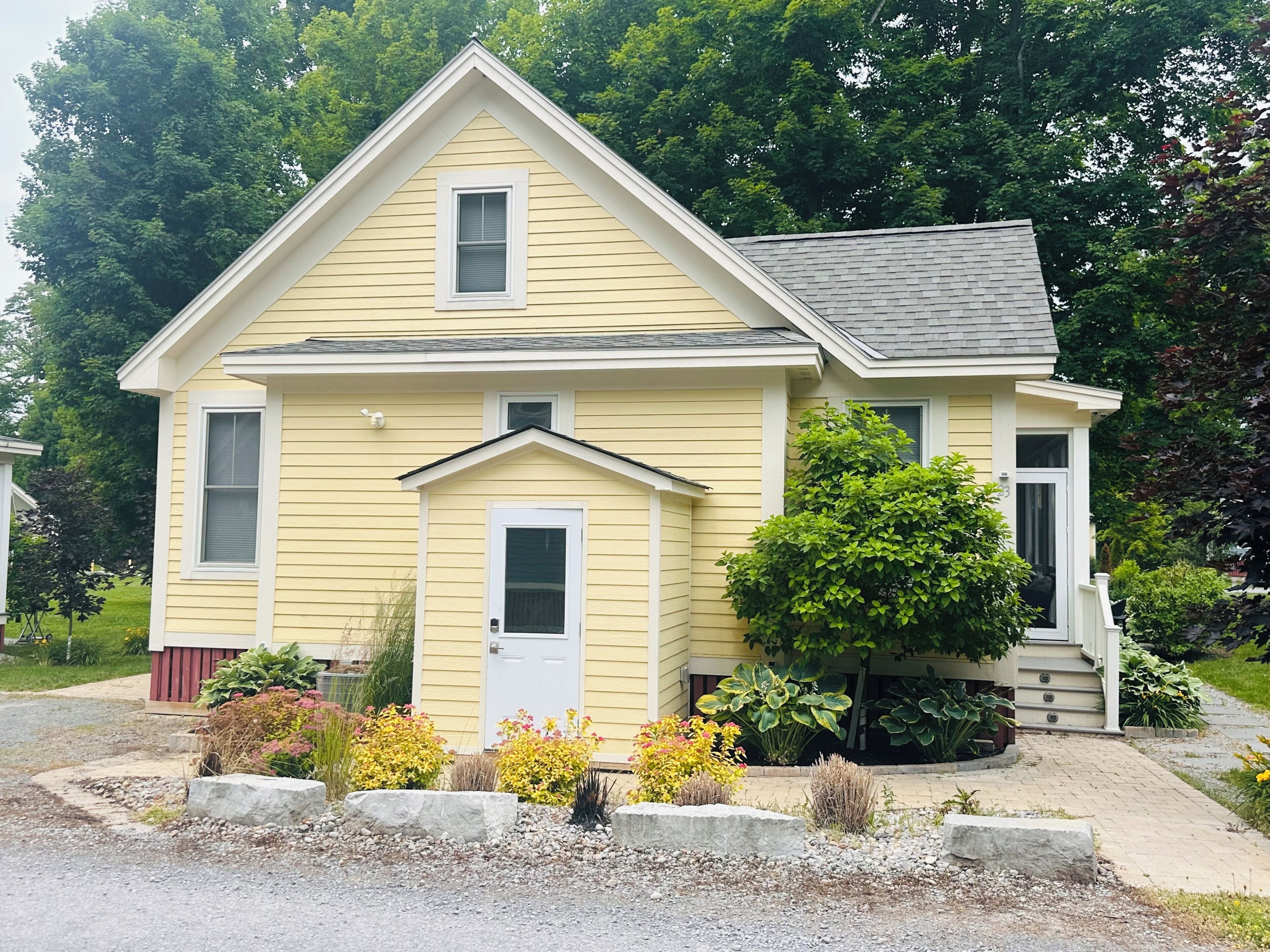 A two-story house with a gabled roof, a front porch, and a small front yard with various plants and a mailbox.