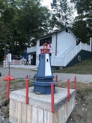 Una maqueta de faro sobre una plataforma de madera, con un edificio blanco al fondo.