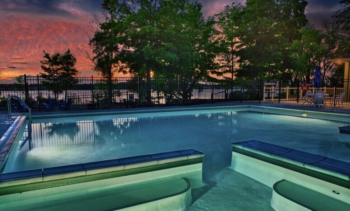 A swimming pool with a view of trees and a sunset.