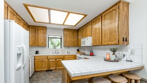 A kitchen with wooden cabinets, a white refrigerator, a microwave, a sink, and a window.