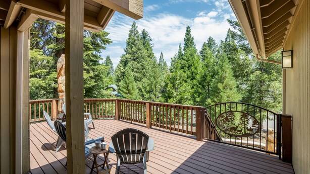 A wooden deck with outdoor furniture, a railing, and a view of dense forest.