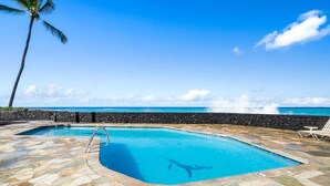 A pool with a stone deck, a palm tree, and a view of the ocean.