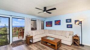 A living room with a large window, a ceiling fan, a sofa, a coffee table, and artwork on the walls.