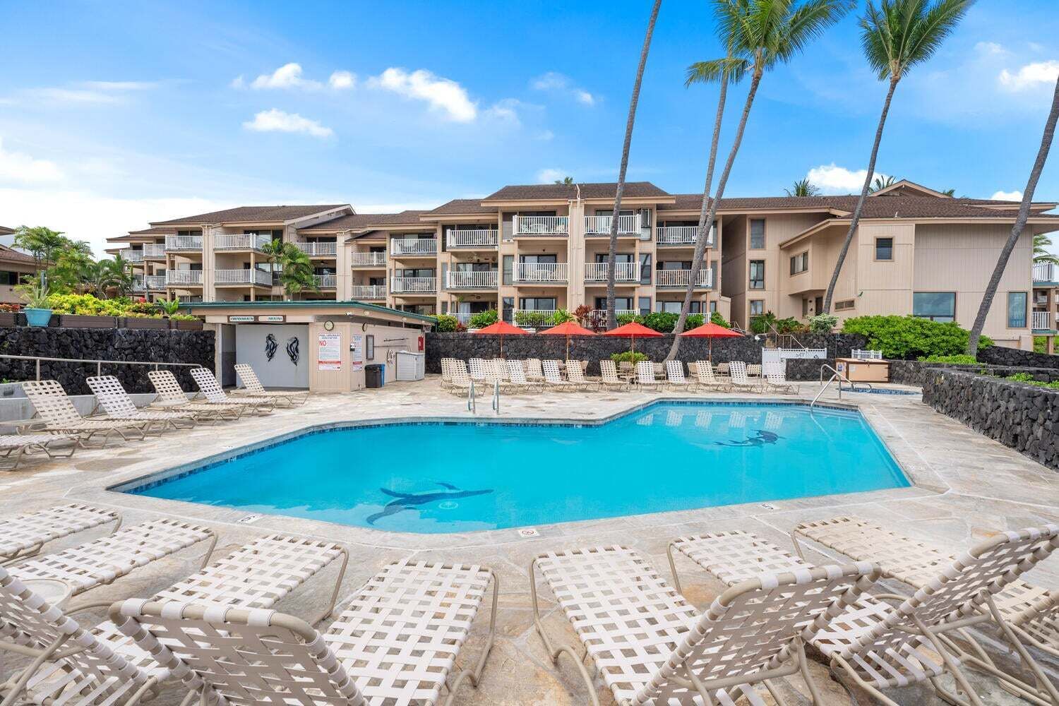 Une piscine avec des chaises longues, un bâtiment doté de balcons et des palmiers.