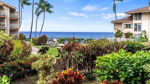 A resort with a view of the ocean, palm trees, and a well-maintained garden.