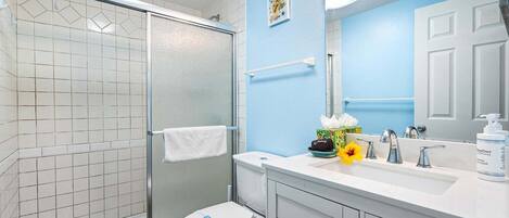 A bathroom with a glass shower enclosure, a white toilet, a sink with a mirror, and a towel rack.