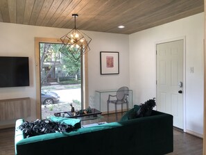 A living room with a green sofa, a glass coffee table, a modern chandelier, and a large window with a view of the street. - Scandinavian Chic Luxury Living In Montrose (Houston)