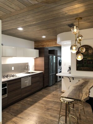 A modern kitchen with stainless steel appliances, wooden cabinetry, and a bar area with stools.
