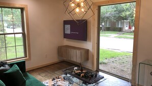 Ett modernt vardagsrum med en grön soffa, ett soffbord i glas med dekorativa föremål, en unik, geometrisk lampa och ett inramat konstverk på väggen.