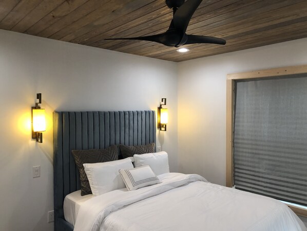 A bedroom with a wooden ceiling, a bed with white bedding, two wall-mounted lights, and a ceiling fan.