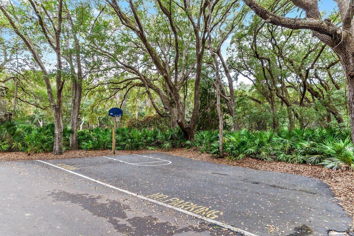 A basketball court with a parking sign and trees in the background.