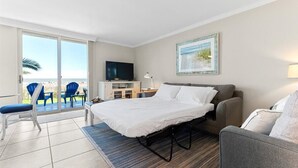 Et hotelværelse med seng, sofa, fjernsyn og en balkon med stole.