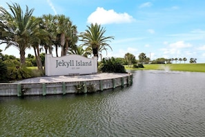 A sign for Jekyll Island with a water feature and palm trees in the background.