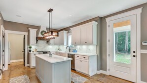 Una cocina moderna con armarios blancos, una isla grande y vistas al exterior a través de una puerta de cristal.