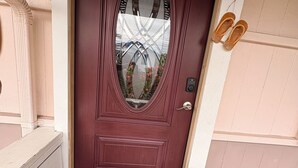 A red door with a glass panel, a doormat with "HOME" written on it, and a pair of shoes on the wall to the right.