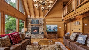 A cozy log cabin interior with a fireplace, leather sofas, and a large TV.