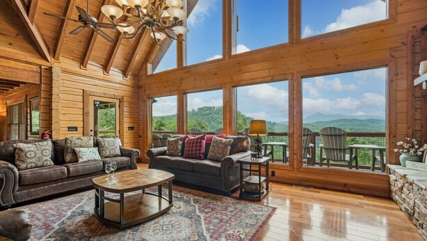 A spacious wooden cabin with a large living area, a fireplace, and a balcony with a scenic mountain view.