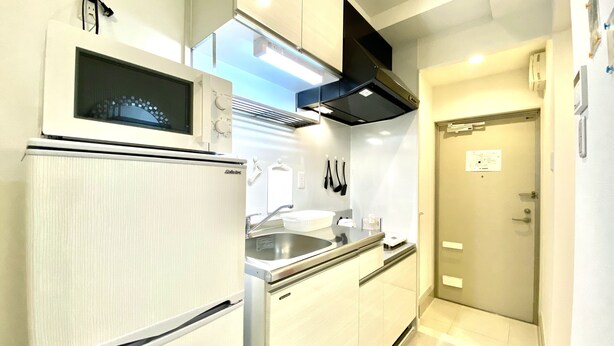A compact kitchen with a built-in microwave, stainless steel sink, and a black range hood. - Le Soleil Asato (Naha)